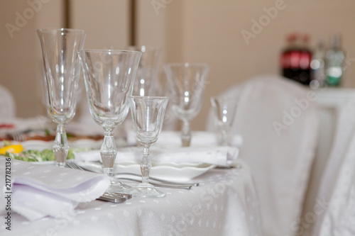 Glasses, flowers, fork, knife, napkin folded in a pyramid, served for dinner in restaurant with cozy interior. Wedding decorations and items for food, arranged by the catering service on a large table