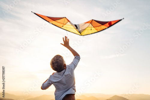 Boy start to fly bright orange kite in the sky photo