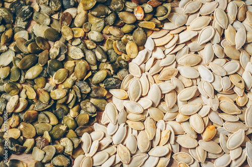 Half of pumpkin seeds peeled from shell, second half in shell, background, texture photo