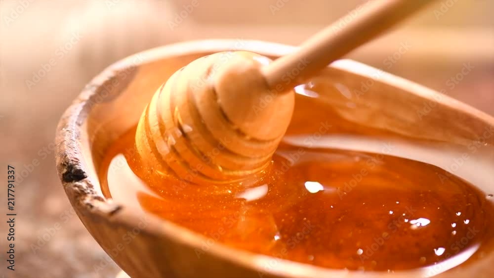 Honey dripping from honey dipper in wooden bowl. Healthy organic thick honey closeup. Slow motion. 3840X2160 4K UHD video footage