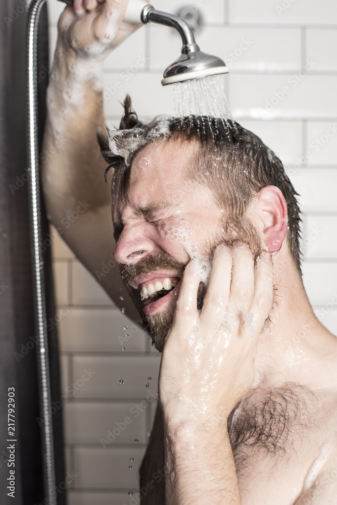 A handsome, bearded man washes the shampoo from his hair in the bathroom with a shower head with warm running water. A handsome, bearded man washes the shampoo from his hair in the bathroom with a shower head with warm running water.