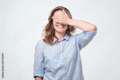 Portrait of pretty caucasian woman with long hair laughing covering her eyes with hand.