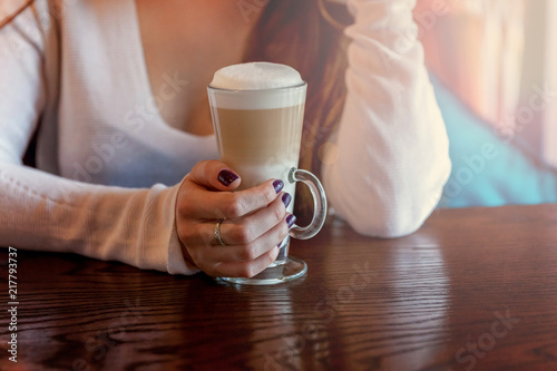 Latte macchiato drink in tall glass close up. Coffee fresh cream cappuccino on table in cafe. Wake up, morning addiction concept photo