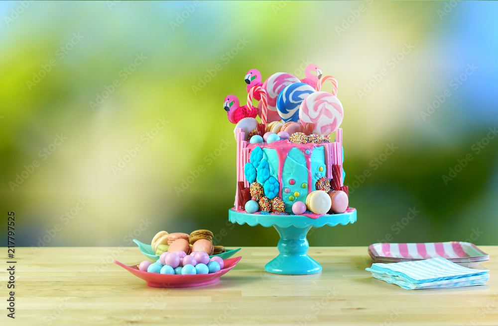 On-trend candyland fantasy drip cake for children's, teen's birthday, anniverary, mother's day and valentine's day celebrations, against bokeh garden background.