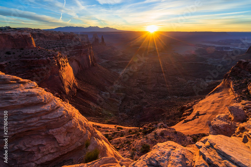 Cliff's-edge sandstone Mesa Arch framing an iconic sunrise view of the red rock canyon landscape below.