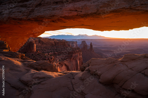 Cliff s-edge sandstone Mesa Arch framing an iconic sunrise view of the red rock canyon landscape below.