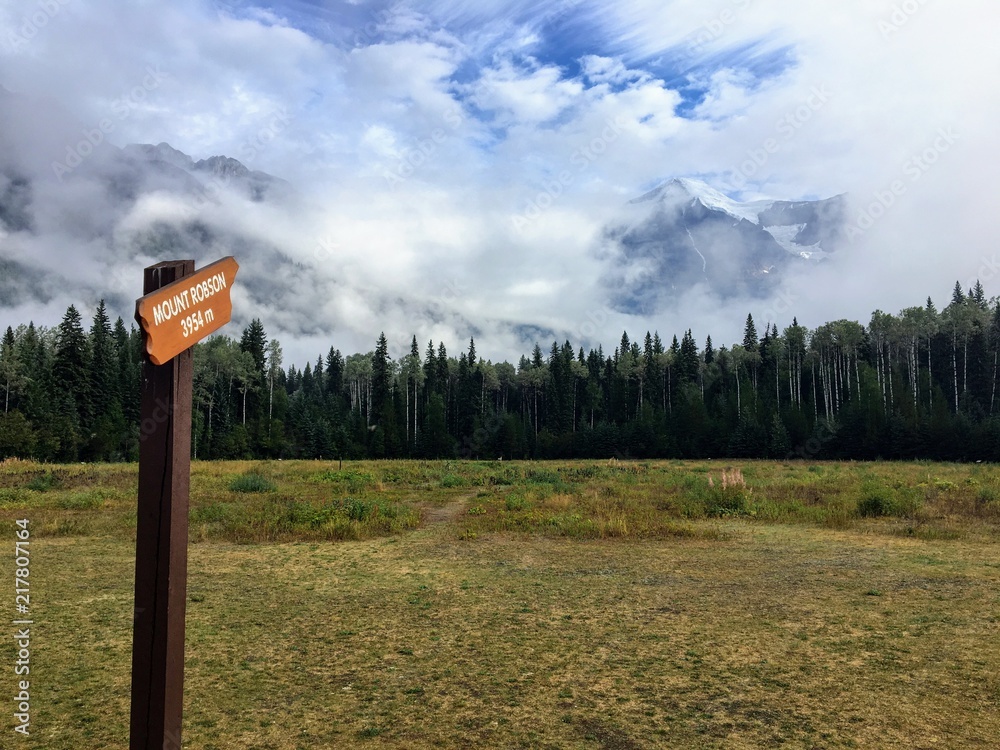 A wood sign labeled Mount Robson and pointing to Mount Robson far off in the distance in beautiful British Columbia, Canada