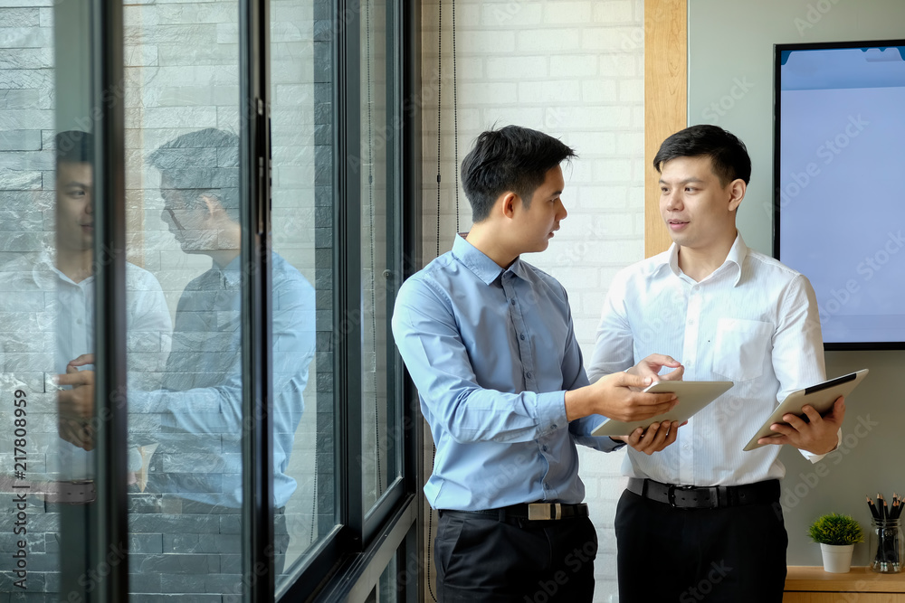 Two coworkers standing in a meeting room looking at a digital tablet Two coworkers standing in a meeting room looking at a digital tablet