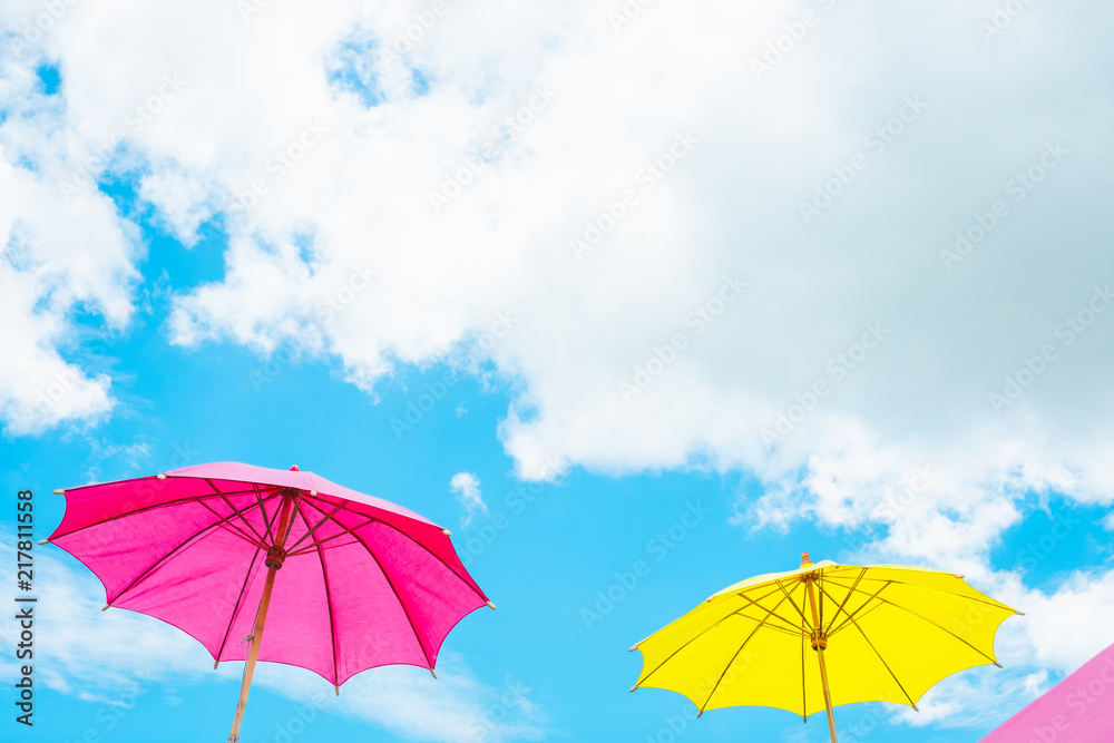 Colorful pink and yellow umbrella with blue sky cloud with copy space.