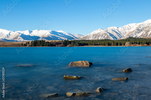 Smooth lake with rocks and snow capped mountains in the background
