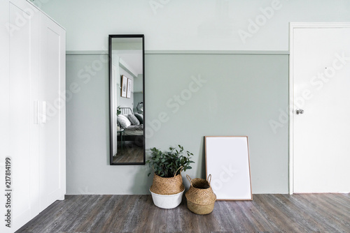 Fototapeta Naklejka Na Ścianę i Meble -  cozy room decoration with artificial plants in the basket and empty frame with full height mirror on green painted wall / decoration idea / cozy apartment / interior design concept