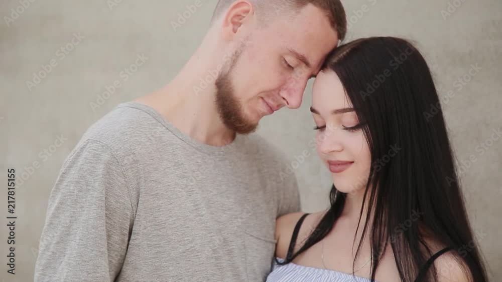 A loving couple hugs and kisses against the background of a concrete wall. A loving couple hugs and kisses against the background of a concrete wall.