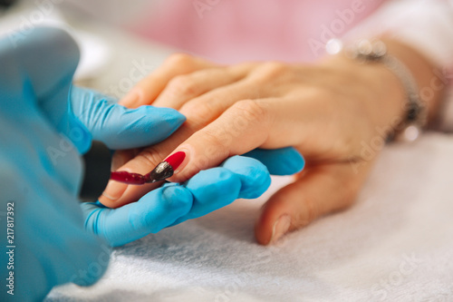 Classic red. Close up of female hands applying nail polish and togging blue gloves