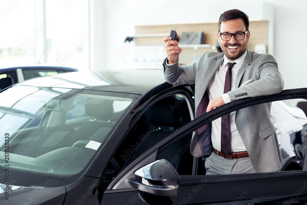 Happy businessman holding keys to her new car at the dealership