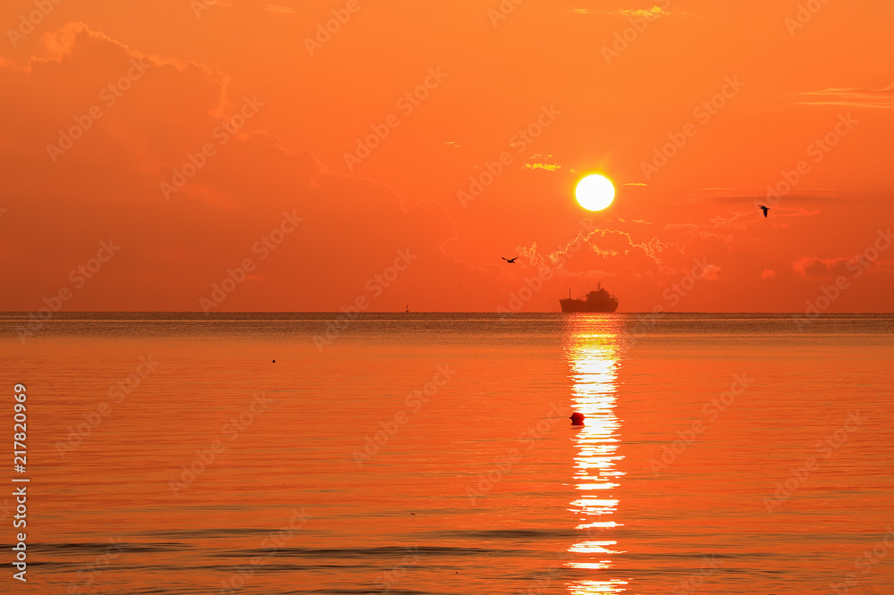 Beautiful red orange sunrise above the sea and clouds with a ship crossing the reflected in the water sun path Beautiful red orange sunrise above the sea and clouds with a ship crossing the reflected in the water sun path