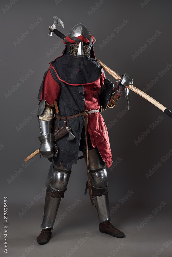 Medieval knight on grey background. Portrait of brutal dirty face warrior with chain mail armour red and black clothes and battle axe Medieval knight on grey background. Portrait of brutal dirty face warrior with chain mail armour red and black clothes and battle axe