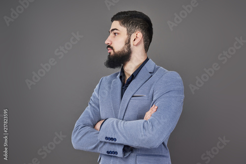 Portrait of freelancer man with beard in jacket standing against gray backdrop