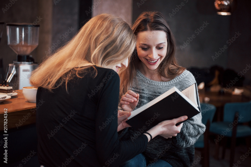Two young women sitting in the cafe drinking coffee and enjoying in good books. Students on coffee break. Education, lifestyle concept Two young women sitting in the cafe drinking coffee and enjoying in good books. Students on coffee break. Education, lifestyle concept