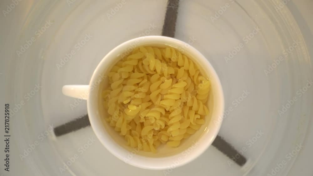 Making microwave mug meal. Boiling pasta in a mug. Microwave macaroni with water top view. Making microwave mug meal. Boiling pasta in a mug. Microwave macaroni with water top view.