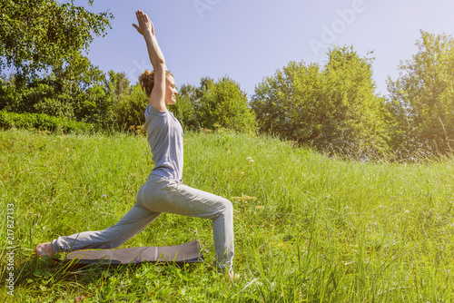 Young attractive woman practicing yoga outdoors on a sunny day, Virabhadrasana, warrior pose