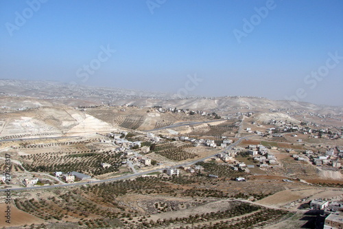 The landscape of the Israeli valleys with small settlements at the foot of the hills in the background of a cloudy blue sky.