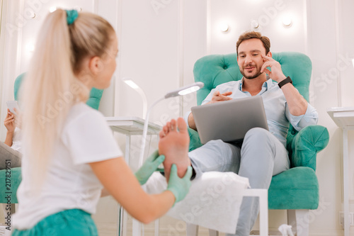 Massage salon. Dark-haired bearded prosperous businessman working distantly while sitting in massage salon