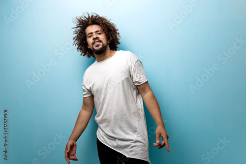 A curly-headed brunet man with flying hair is wearing an asymmetric white T-shirt. Easy-going character and contended look.