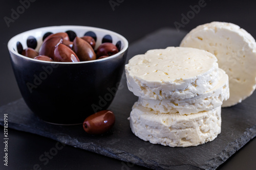 Feta cheese on black background with bowls of black olive with selective focus on cheese