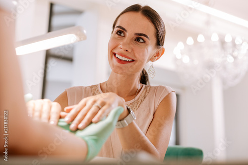 Looking at master. Dark-haired charming woman wearing fashionable beige blouse looking at her nail master photo