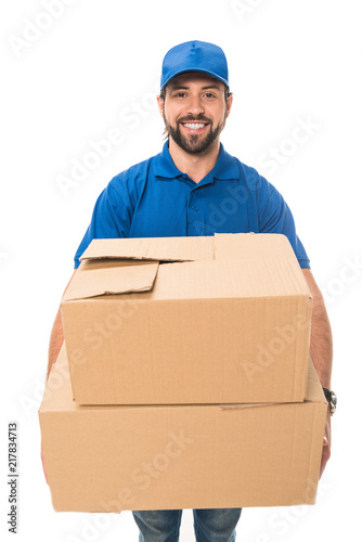 handsome happy young delivery man holding cardboard boxes and smiling at camera isolated on white © LIGHTFIELD STUDIOS