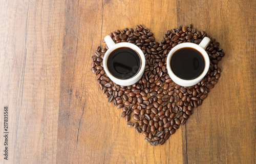A cup of coffee and Heart-shaped coffee beans on wooden table background