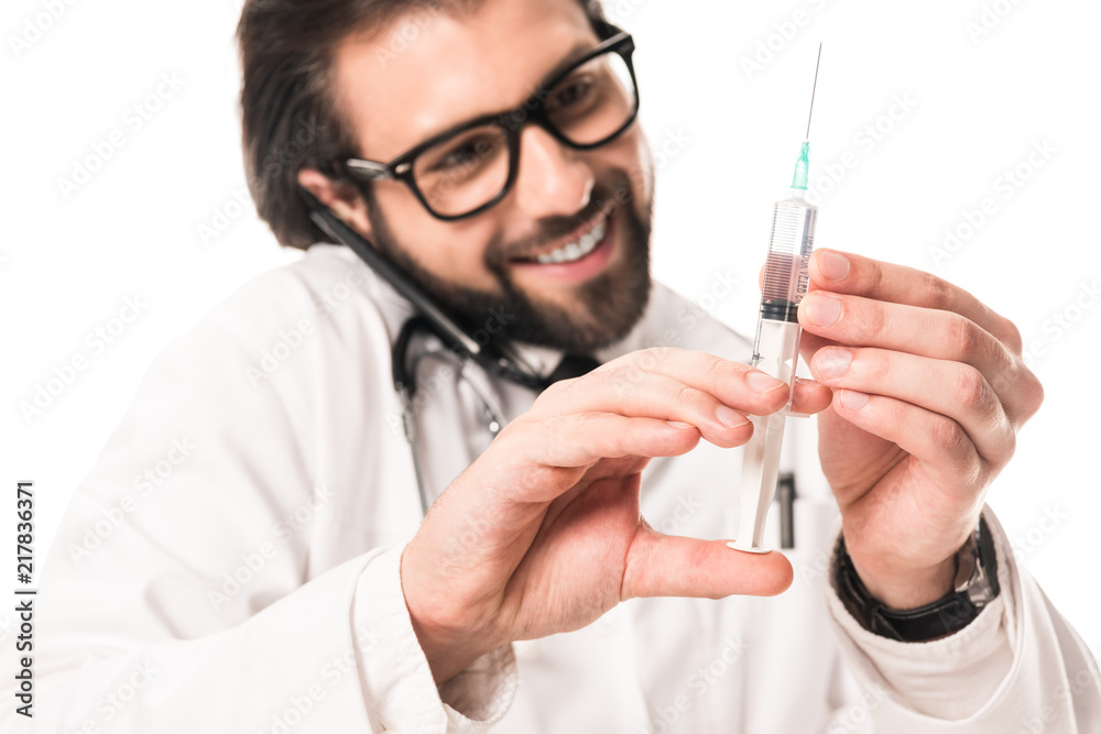 smiling doctor holding syringe and talking by smartphone isolated on white smiling doctor holding syringe and talking by smartphone isolated on white