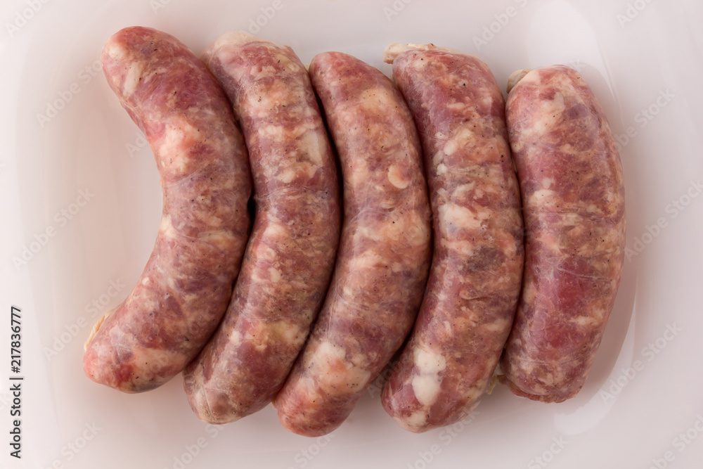 Raw sausages for a barbecue on a white plate. Several barbecue sausages lie next to each other. Raw sausages for a barbecue on a white plate. Several barbecue sausages lie next to each other.