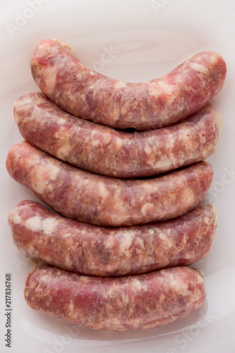 Raw sausages for a barbecue on a white plate. Several barbecue sausages lie next to each other.