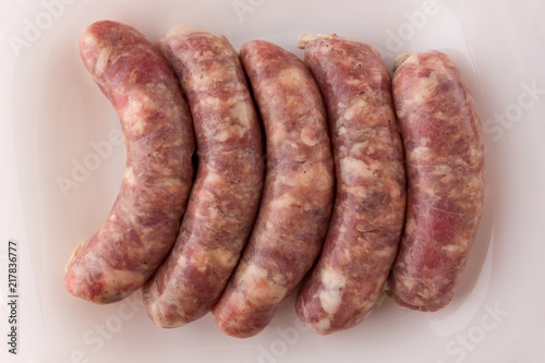 Raw sausages for a barbecue on a white plate. Several barbecue sausages lie next to each other.