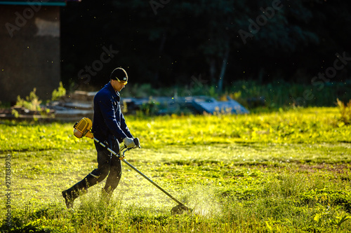 Young guy mows the grass trimmer