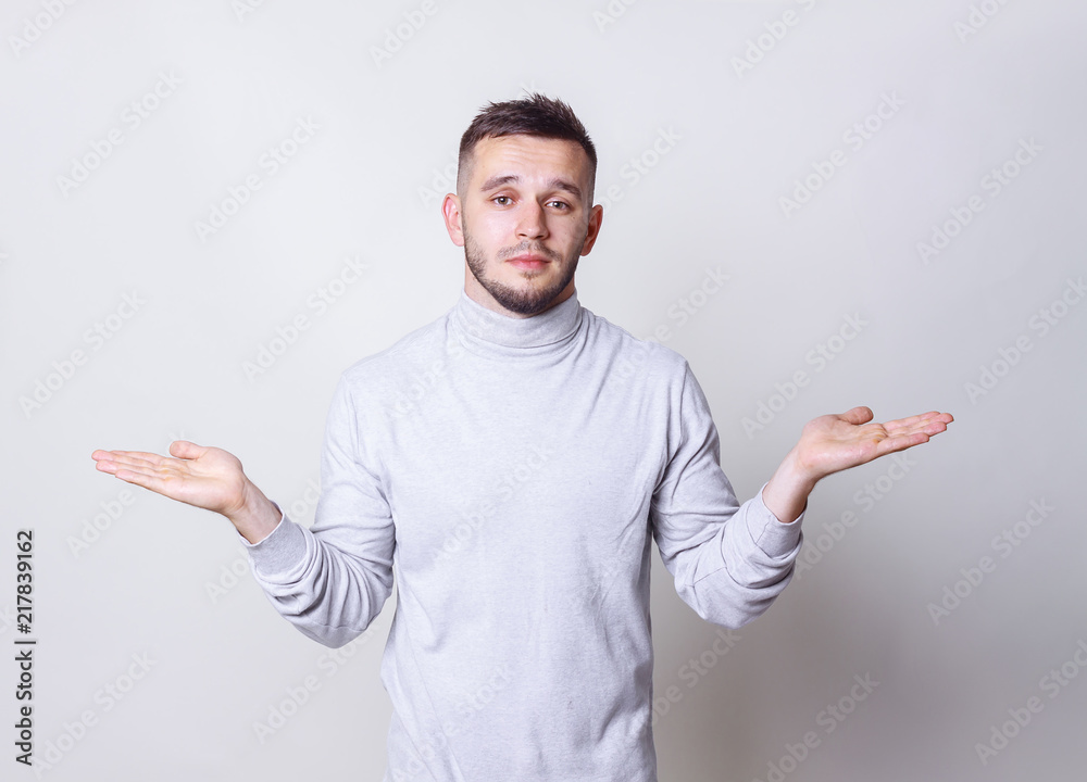 Young man raises hands palms up show or demonstrating something on grey background copy space Young man raises hands palms up show or demonstrating something on grey background copy space