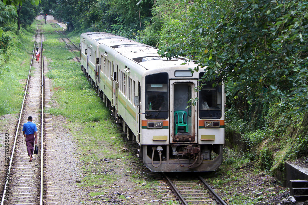Naklejka premium Pociąg jedzie po torze. za wieśniakiem Myanmarese idącym równoległym torem kolejowym.