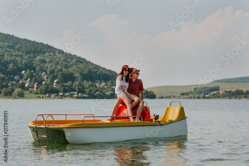 Portrait of smiling couple in love having fun pedal boating on hot summer day. Full length of young happy man and woman sitting on pedal boat. © Newman Studio