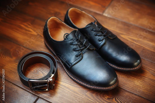 Black leather male shoes and belt on wooden background