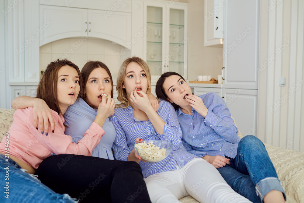 Young girls watching TV, eating popcorn sitting on the couch in the room. Young girls watching TV, eating popcorn sitting on the couch in the room.
