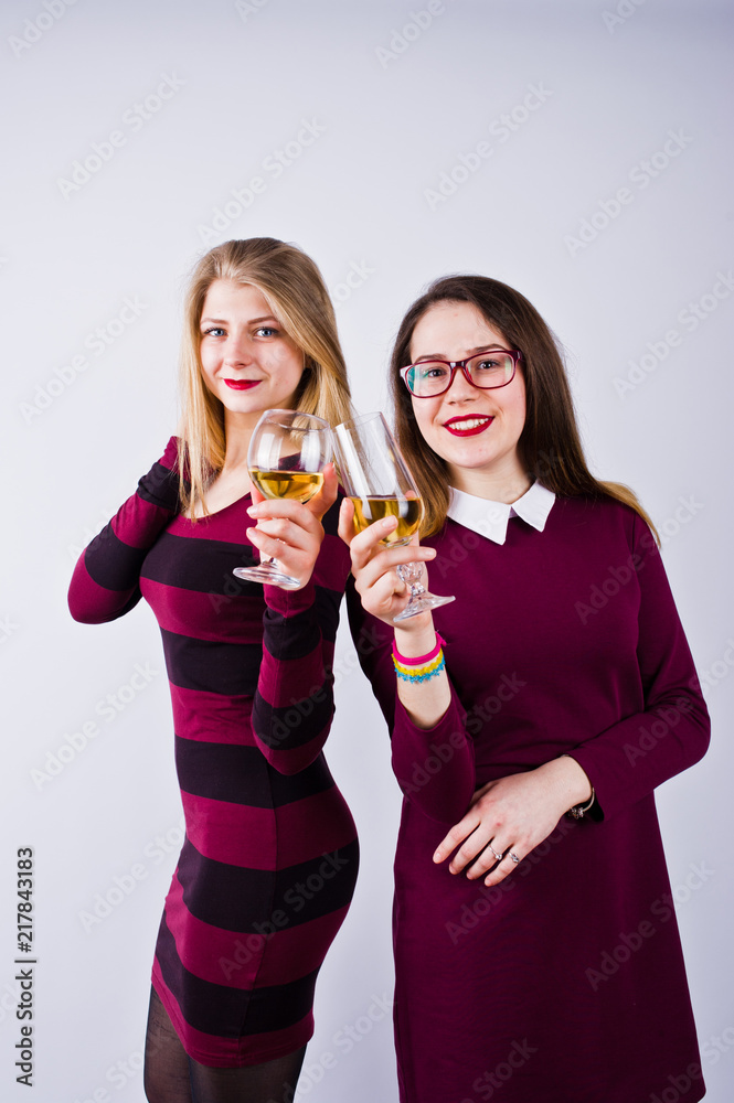 Two attractive friends in purple dresses drink sparkling wine or champagne in the studio. Two attractive friends in purple dresses drink sparkling wine or champagne in the studio.