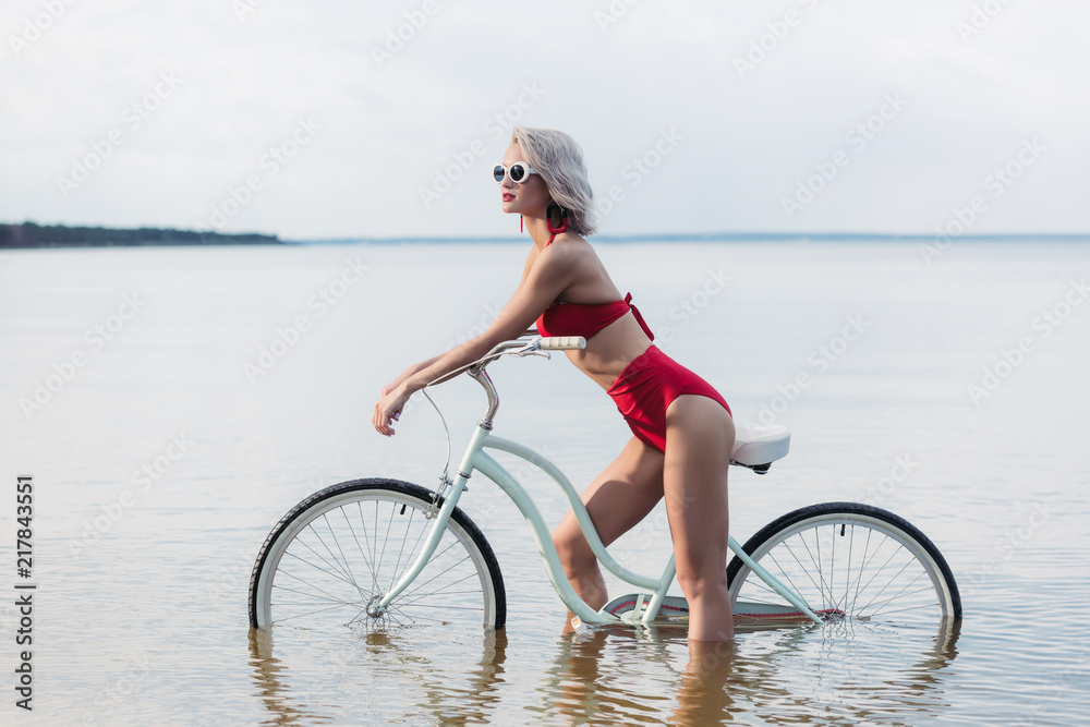 beautiful fashionable girl in red bikini sitting on bike in water beautiful fashionable girl in red bikini sitting on bike in water