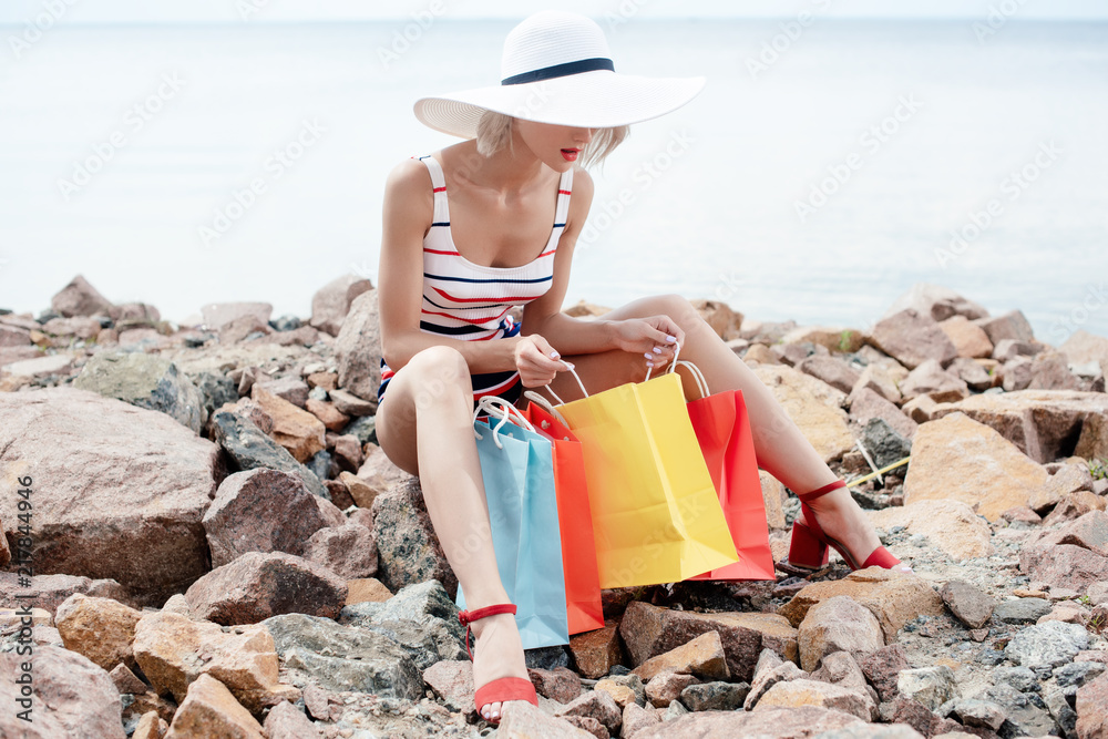 beautiful woman in white hat sitting on rocky beach with shopping bags