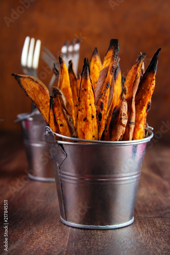 Homemade baked sweet potato fries with skin in  metal serving bucket on wooden background