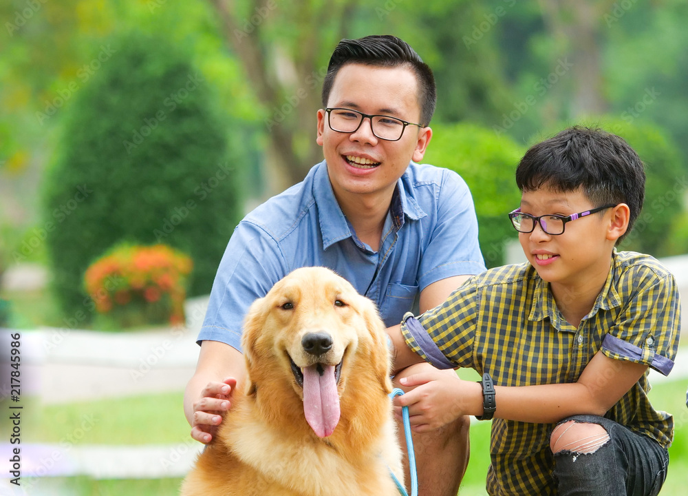 Little asian boy and his father playing with a cute golden retriever dog in the park.