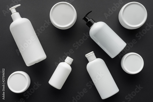 top view of scattered white bottles of cream isolated on black, beauty concept