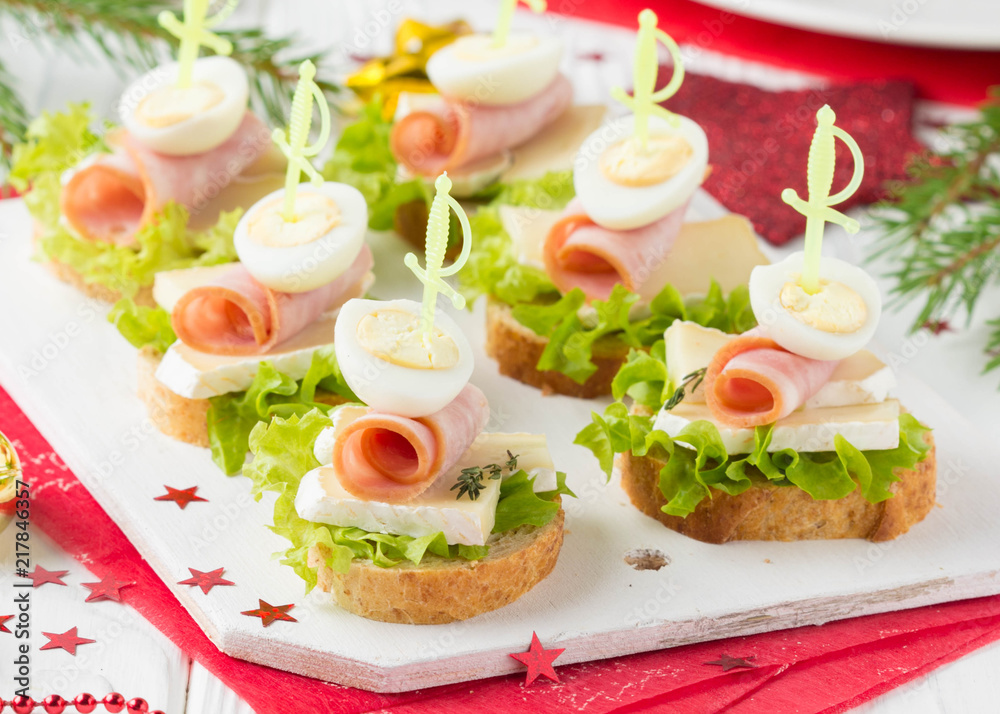Christmas canapes on bread with brie or Camembert cheese, ham and boiled quail egg. Beautiful presentation on the festive new year's table. Delicious starter