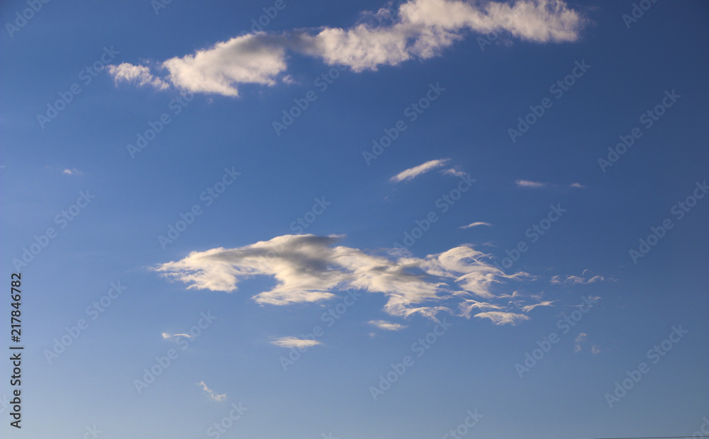 the evening blue sky with white clouds. the sun hides behind the clouds. rays of the sun at sunset illuminate different colors of fluffy clouds.