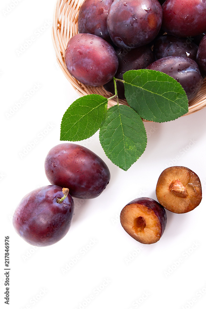 Yellow wooden basket with ripe plums, whole and half ripe plums isolated on a white background.. Yellow wooden basket with ripe plums, whole and half ripe plums isolated on a white background..